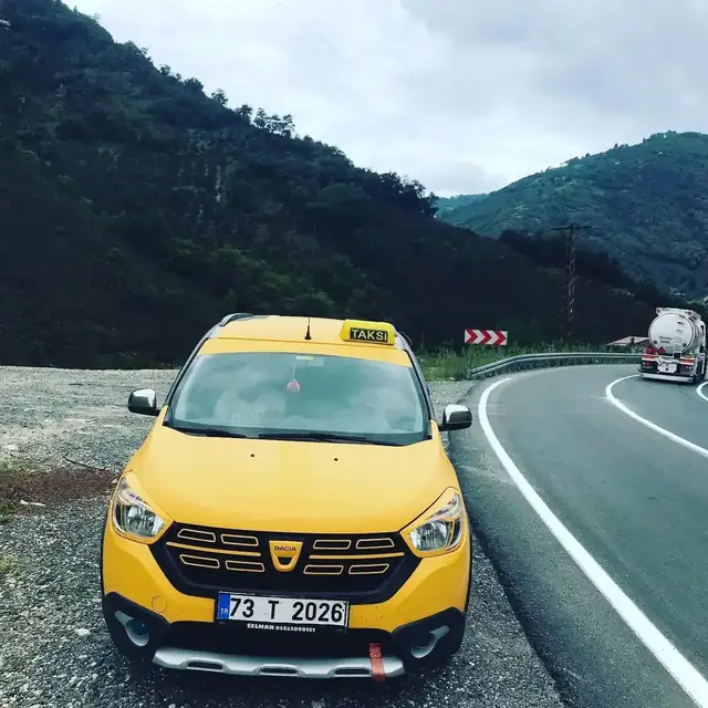 Dağlık bir yolda park hâlindeki sarı taksi